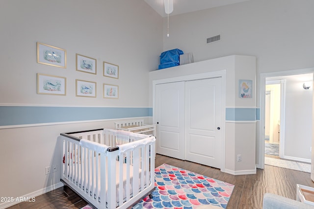bedroom with baseboards, a high ceiling, visible vents, a closet, and wood finished floors