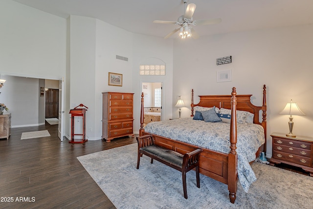 bedroom with connected bathroom, dark wood finished floors, baseboards, visible vents, and a towering ceiling