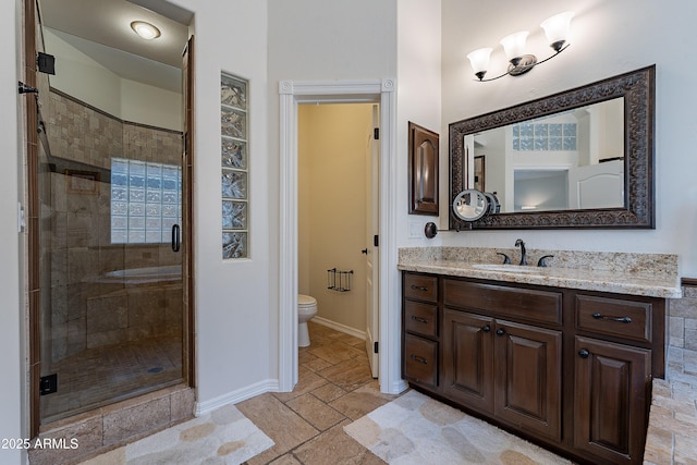 full bath with vanity, stone tile floors, toilet, baseboards, and a shower stall