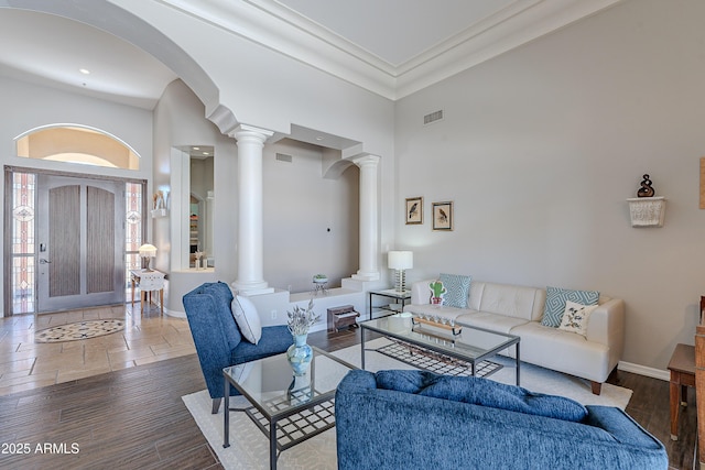 living area with wood finished floors, baseboards, visible vents, a towering ceiling, and ornate columns