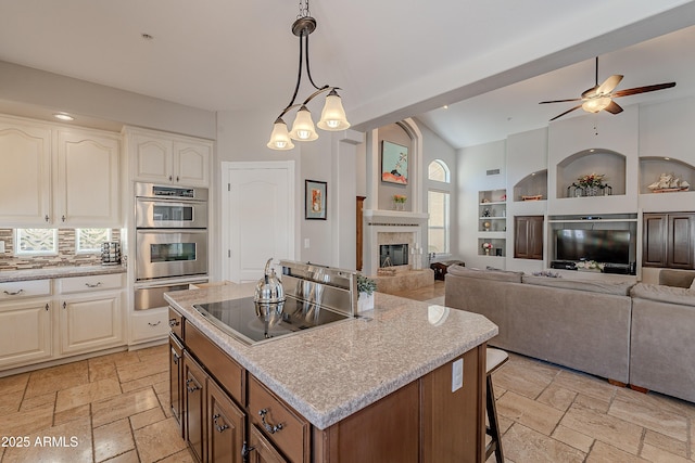 kitchen with black electric cooktop, double oven, a kitchen island, stone tile flooring, and a fireplace