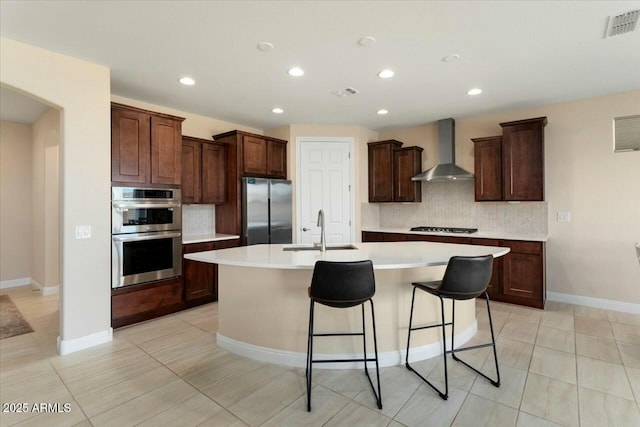 kitchen featuring backsplash, a kitchen island with sink, wall chimney range hood, sink, and appliances with stainless steel finishes