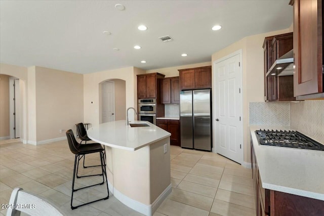 kitchen with stainless steel appliances, an island with sink, a kitchen bar, decorative backsplash, and light tile patterned floors