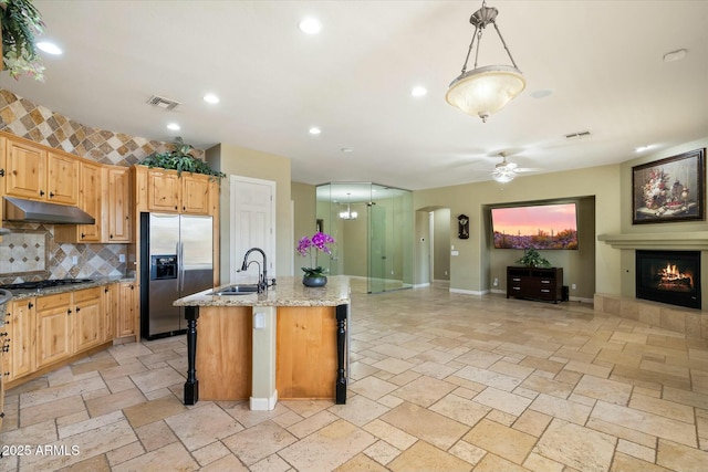 kitchen with under cabinet range hood, visible vents, stainless steel refrigerator with ice dispenser, and stone tile floors