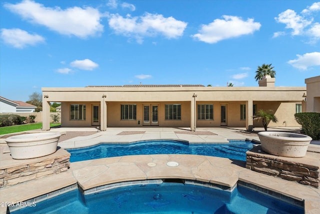 rear view of property with an in ground hot tub, french doors, a patio, and stucco siding