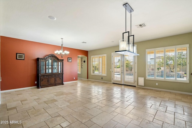 unfurnished dining area featuring stone tile flooring, an inviting chandelier, visible vents, and baseboards