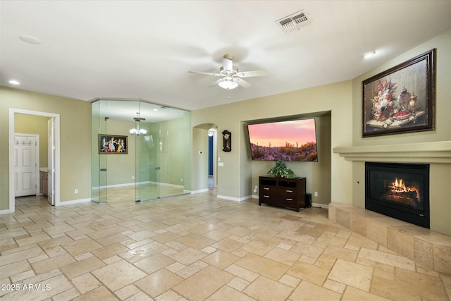 unfurnished living room with a glass covered fireplace, stone tile flooring, visible vents, and baseboards