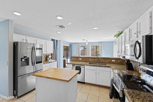 kitchen with appliances with stainless steel finishes, white cabinets, a kitchen island, sink, and wood counters