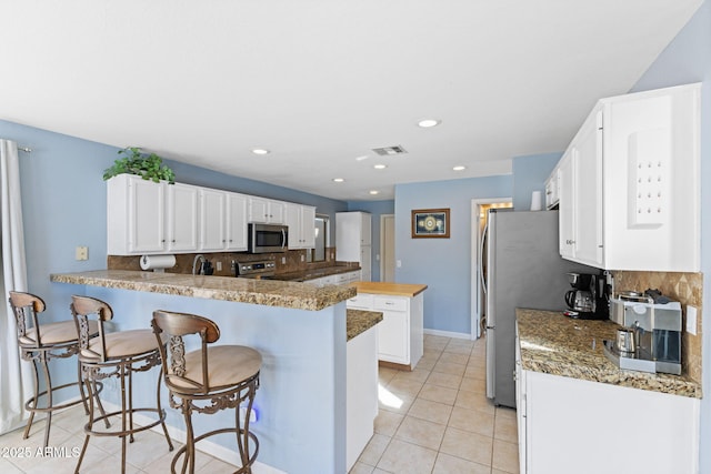 kitchen featuring kitchen peninsula, appliances with stainless steel finishes, backsplash, white cabinets, and light tile patterned floors