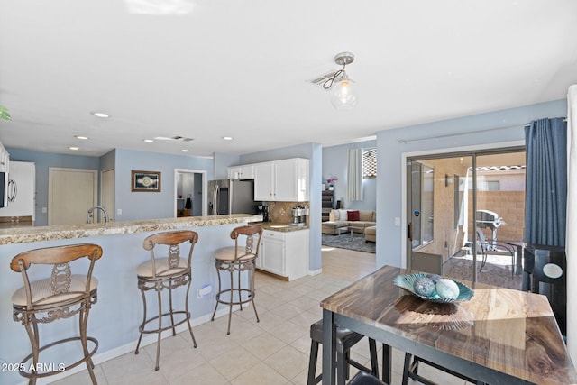 kitchen featuring white cabinetry, decorative backsplash, light stone countertops, a breakfast bar area, and stainless steel refrigerator