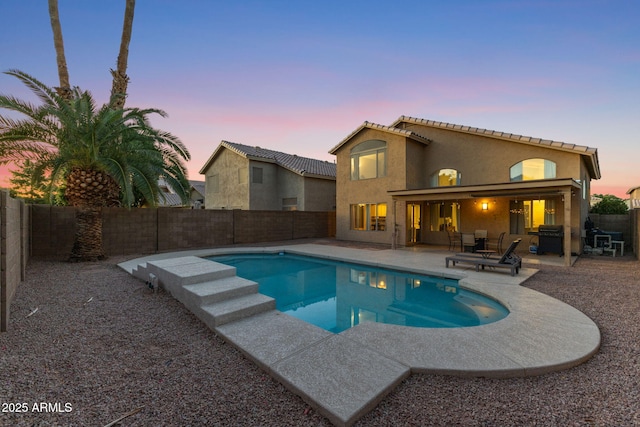 pool at dusk with a patio area and area for grilling