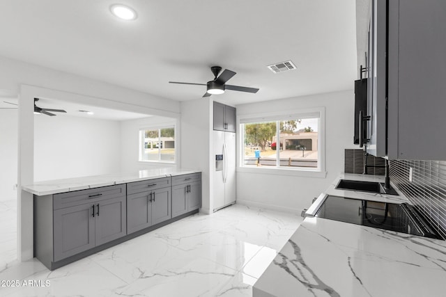 kitchen with light stone counters, a healthy amount of sunlight, gray cabinets, and white fridge with ice dispenser