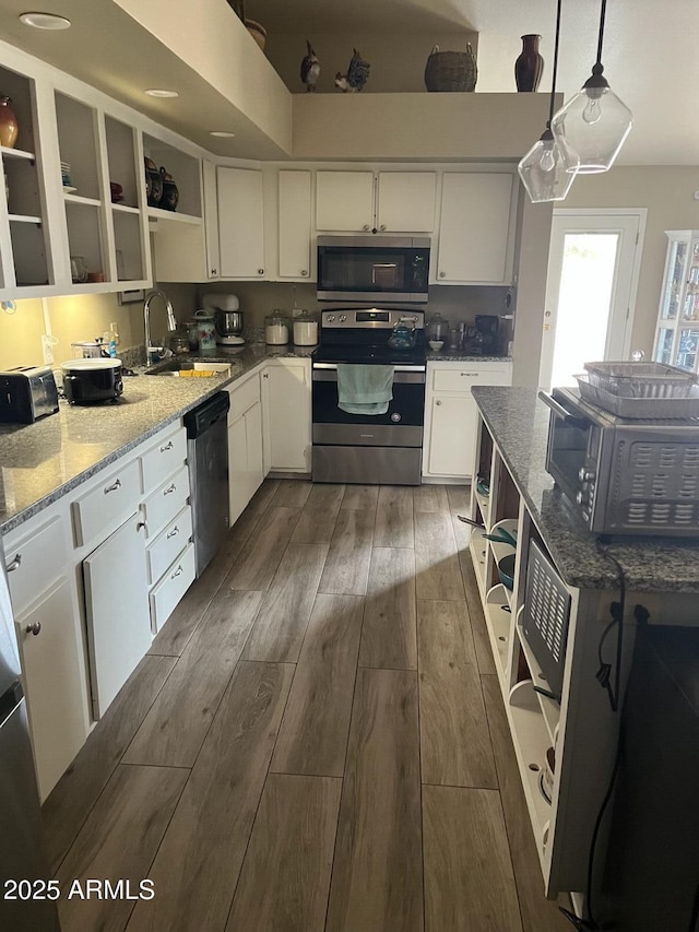 kitchen with sink, appliances with stainless steel finishes, light stone countertops, white cabinets, and decorative light fixtures
