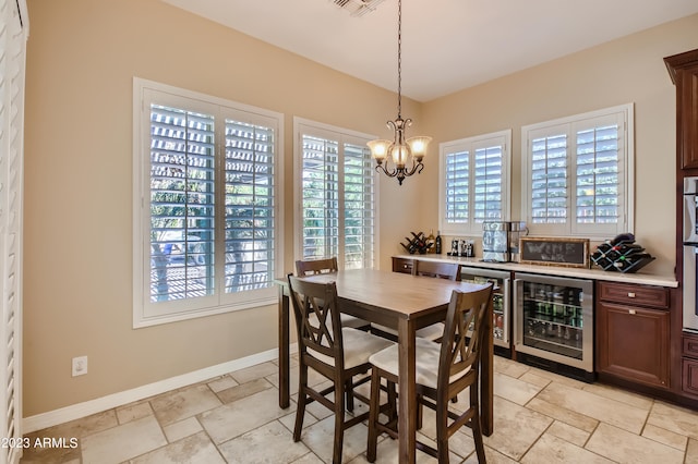 dining area with beverage cooler, a notable chandelier, stone tile flooring, and baseboards