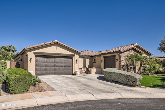 mediterranean / spanish-style home with a garage, stone siding, a tiled roof, and stucco siding