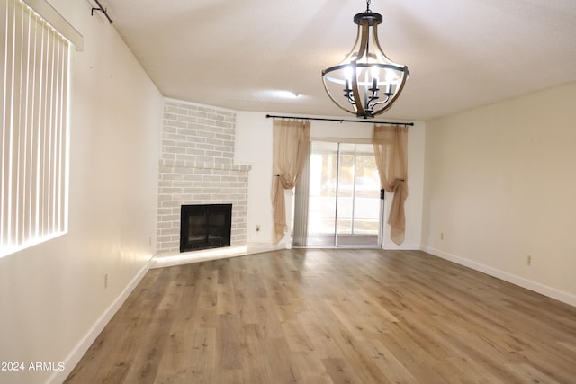 unfurnished living room featuring a brick fireplace, an inviting chandelier, hardwood / wood-style floors, and a textured ceiling