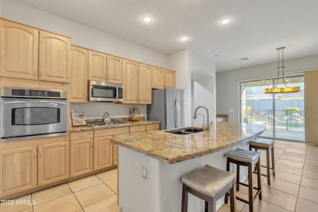 kitchen featuring sink, a kitchen island with sink, stainless steel appliances, light stone countertops, and decorative light fixtures