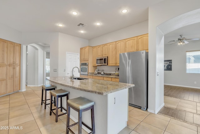 kitchen with sink, a center island with sink, stainless steel appliances, light stone counters, and light tile patterned flooring