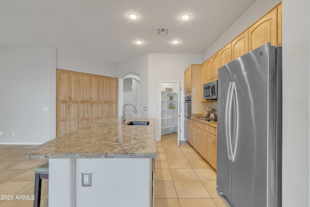 kitchen with sink, light brown cabinets, light tile patterned floors, appliances with stainless steel finishes, and a kitchen island with sink