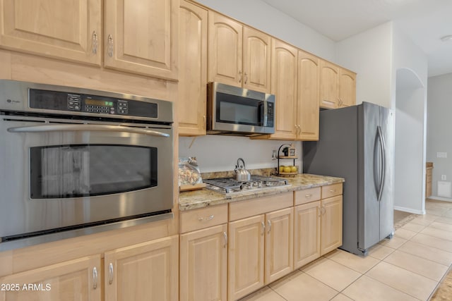 kitchen featuring light stone counters, appliances with stainless steel finishes, light brown cabinetry, and light tile patterned floors