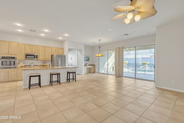 kitchen with light brown cabinetry, light tile patterned floors, a kitchen island, and appliances with stainless steel finishes