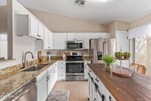 kitchen with stainless steel appliances, visible vents, light tile patterned flooring, a sink, and dark stone counters