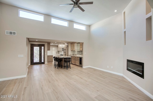 living room featuring beverage cooler, ceiling fan with notable chandelier, a high ceiling, and light wood-type flooring