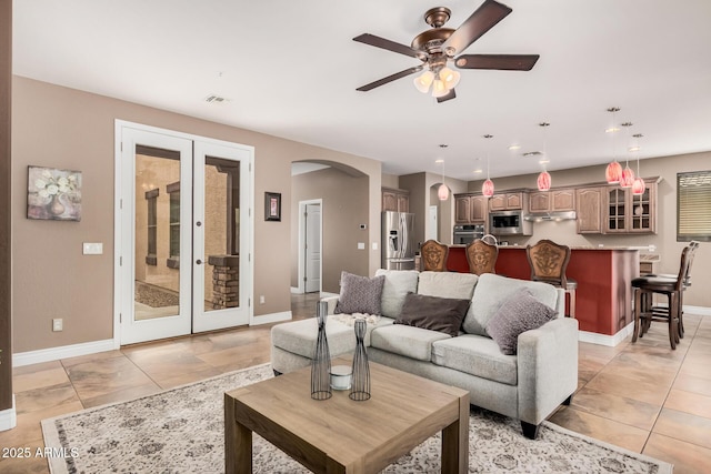 living room featuring baseboards, french doors, light tile patterned flooring, arched walkways, and a ceiling fan