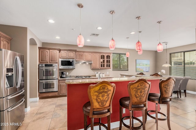 kitchen featuring visible vents, a kitchen island with sink, arched walkways, appliances with stainless steel finishes, and a kitchen bar