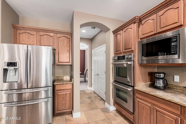 kitchen featuring visible vents, light stone counters, appliances with stainless steel finishes, light tile patterned flooring, and arched walkways