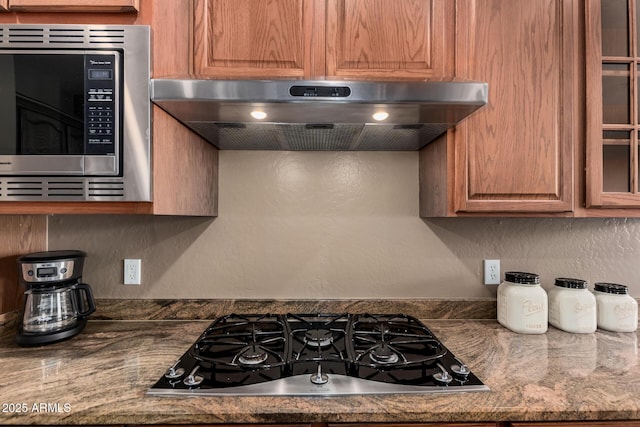 kitchen with a textured wall, stainless steel microwave, extractor fan, and gas stovetop