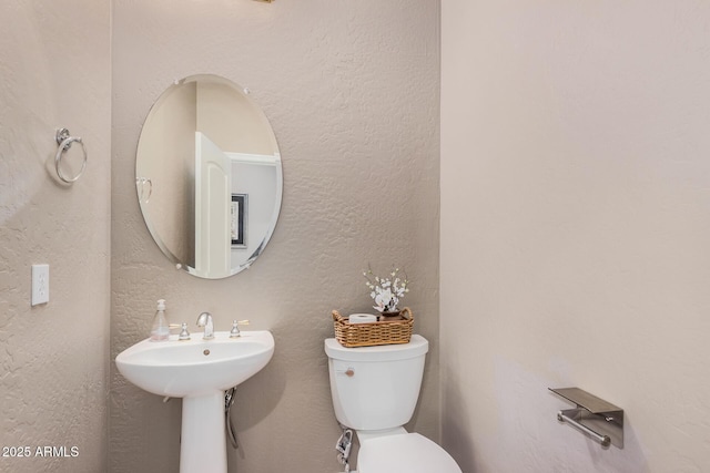 half bathroom with a sink, toilet, and a textured wall