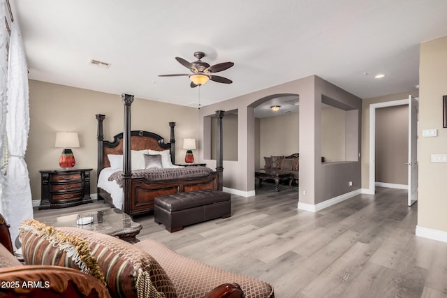 bedroom featuring wood finished floors, visible vents, arched walkways, and baseboards