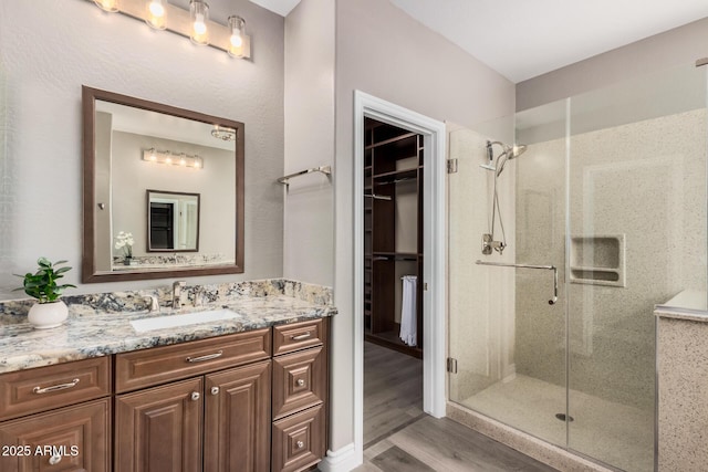 bathroom with a spacious closet, a shower stall, vanity, and wood finished floors