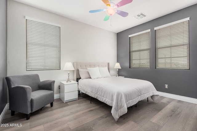 bedroom with a ceiling fan, wood finished floors, visible vents, and baseboards