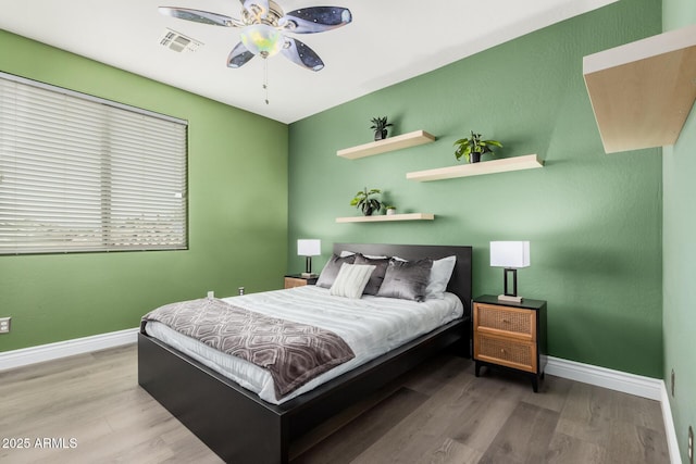 bedroom with ceiling fan, wood finished floors, visible vents, and baseboards