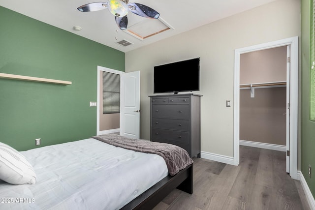 bedroom featuring a walk in closet, attic access, wood finished floors, and baseboards