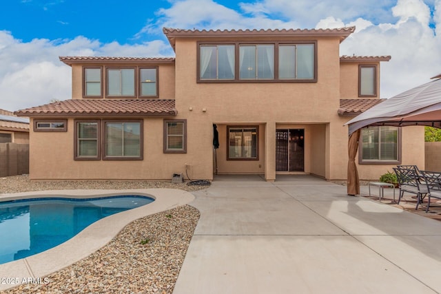 rear view of house with stucco siding, fence, a gazebo, a fenced in pool, and a patio area