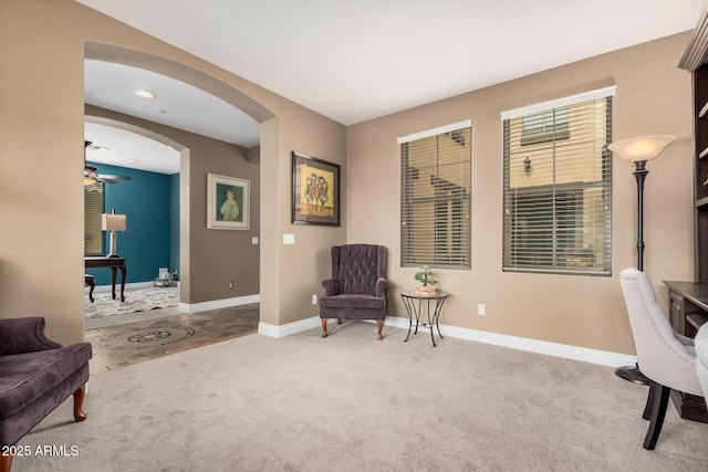 living area with arched walkways, baseboards, carpet, and a ceiling fan