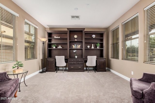 home office with baseboards, visible vents, built in desk, and light carpet