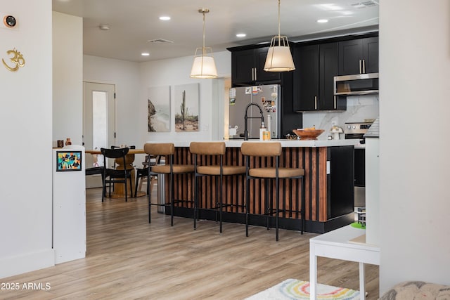 kitchen featuring light wood-style flooring, stainless steel appliances, dark cabinetry, and light countertops