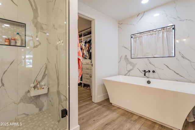 full bath with a freestanding tub, a spacious closet, a marble finish shower, and wood finished floors