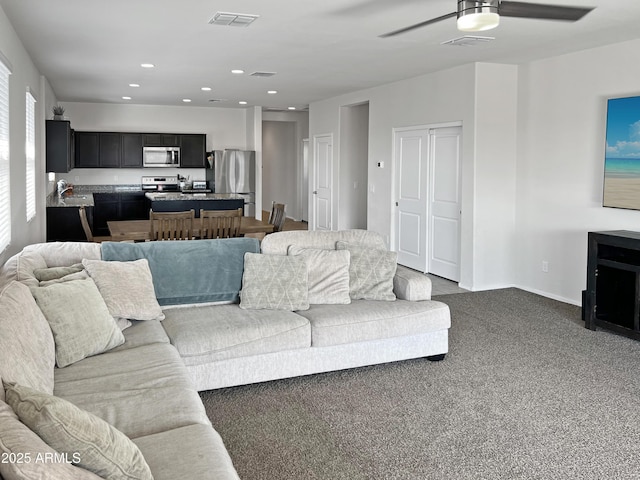 living room featuring dark colored carpet, sink, and ceiling fan