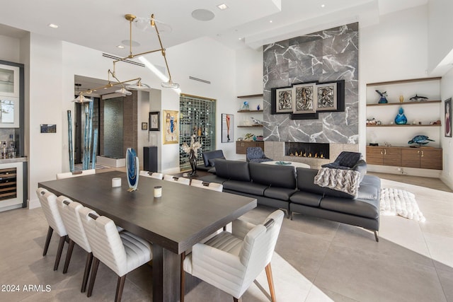 dining space with beverage cooler, light tile flooring, a towering ceiling, and a fireplace