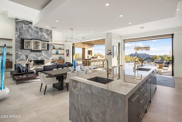 kitchen featuring sink, light tile flooring, an island with sink, and light stone counters