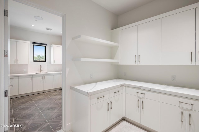 kitchen featuring tile flooring, light stone counters, white cabinets, and sink