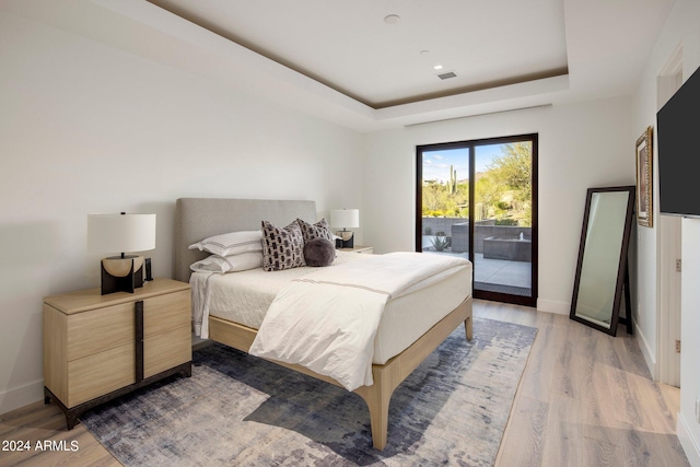 bedroom featuring hardwood / wood-style flooring, a raised ceiling, and access to exterior