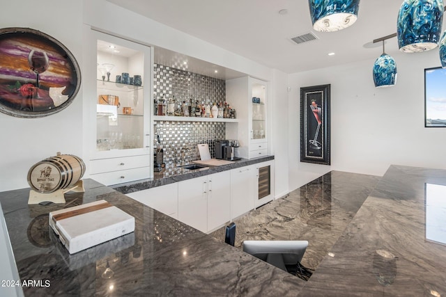 bar featuring beverage cooler, white cabinets, sink, tasteful backsplash, and dark stone counters