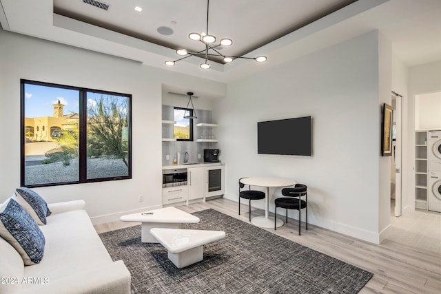 tiled living room featuring sink, an inviting chandelier, stacked washer / dryer, and a raised ceiling