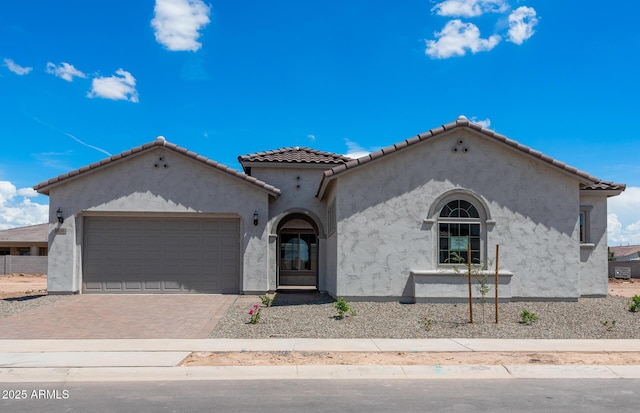 mediterranean / spanish-style home featuring decorative driveway, a tiled roof, an attached garage, and stucco siding